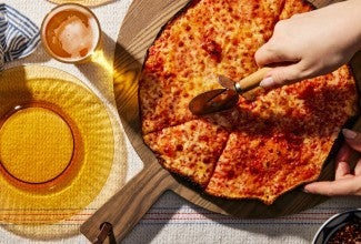 Overhead shot of hand using a pizza cutter to slice the pizza. 